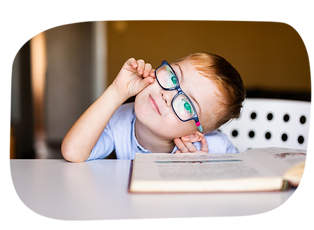 A cute kindergarten-age Caucasian boy with a learning difference adjusts his glasses while he reads a book